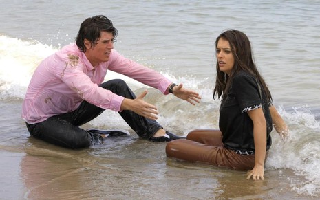 Pedro Lemos grava com camisa rosa e molhado ao lado de Lisandra Parede, sentada na areia com cara de desespero, como Tobias e Maria Cecília