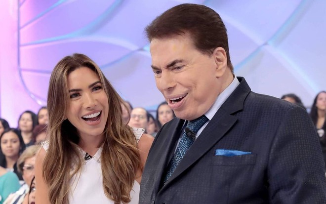 Patricia Abravanel sorri enquanto observa Silvio Santos; os dois estão no centro do auditório do Programa Silvio Santos