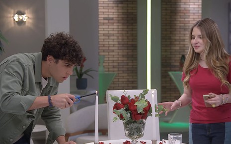 Igor Jansen, caracterizado como João, e Sophia Valverde, a Poliana, preparam uma mesa de jantar em cena de Poliana Moça
