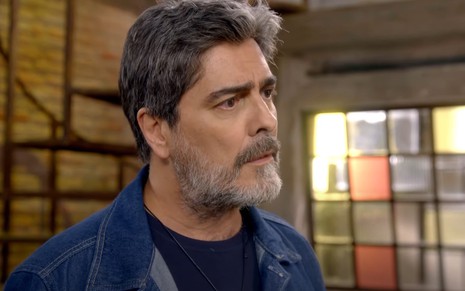 Renato (Junno Andrade) de camiseta preta e camisa jeans por cima com expressão séria em cena de Poliana Moça