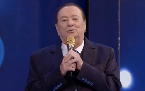 O apresentador Raul Gil segura um microfone dourado no palco do Programa Raul Gil