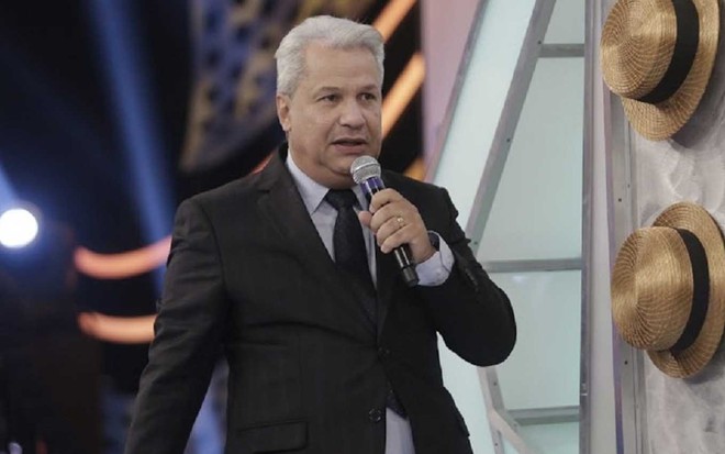 O jornalista Sikêra Júnior está no palco do Programa Raul Gil diante de um display com chapéus de palha
