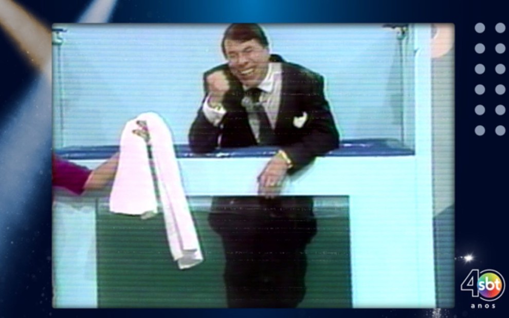 Foto do apresentador Silvio Santos no palco do programa Topa Tudo Por Dinheiro, do SBT, em 1992; ele aparece molhado e prestes a receber uma toalha