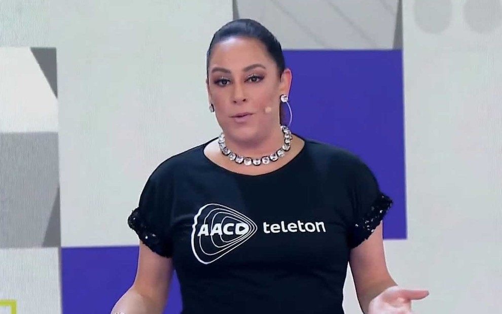 A apresentador Silvia Abravanel com uma blusa preta escrita AACD Teleton no palco do Teleton