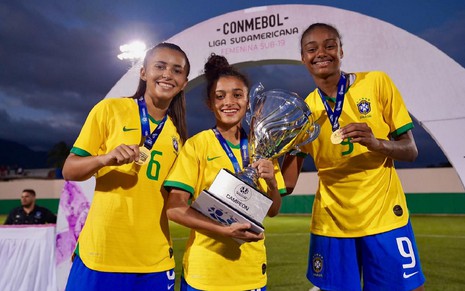 Gisseli, Mariza e Marta com a camisa da Seleção Brasileira, segurando um troféu sub-19