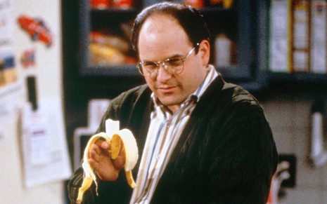 Jason Alexander como o personagem George Costanza em cena de Seinfeld; ele está segurando uma banana