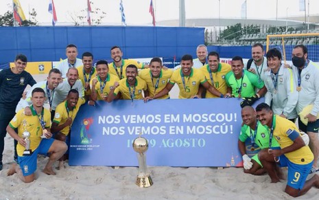 Seleção Brasileira de futebol de areia comemora o título das Eliminatórias da Copa do Mundo da modalidade, disputada no início do ano. Eles usam a camisa amarela do Brasil e sorriem para foto.