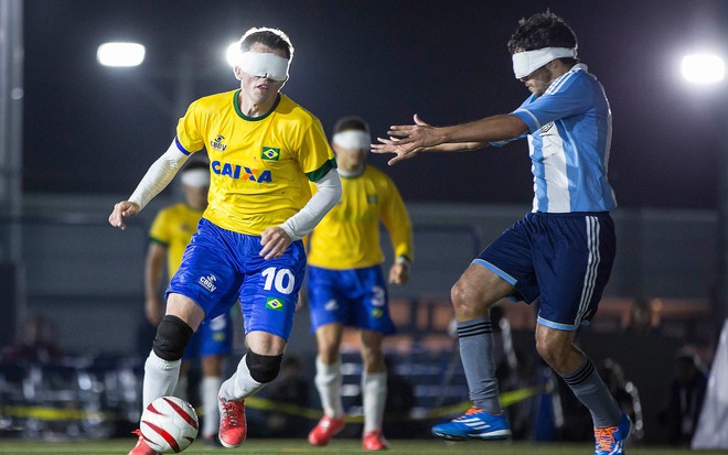 Jogador de futebol de 5 da Seleção Brasileira. Ele está com uma venda e joga contra a Argentina, na modalidade adaptada para deficientes visuais