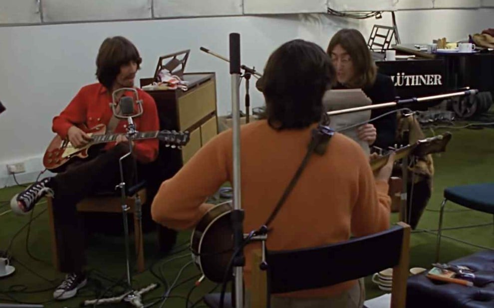Integrantes dos Beatles reunidos em sala de gravação segurando instrumentos sentados virados uns para os outros em centa de The Beatles: Get Back, do Disney+