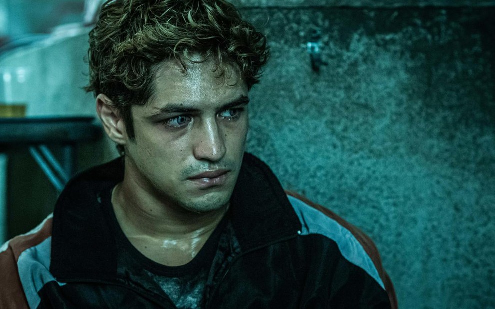 Pedro Dantas (Gabriel Leone) de jaqueta escura no lado esquerdo olha para o lado direito em direção de uma parede em cena da série Dom