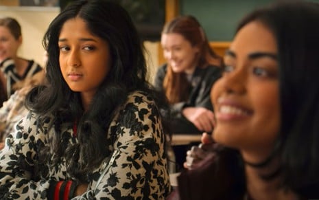 Devi (Maitreyi Ramakrishnan) no lado esquerdo olha para Aneesa (Megan Suri) no lado direito desfocada em sala de aula em cena da série Eu Nunca...