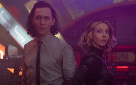 Loki (Tom Hiddleston) de camisa clara e gravata preta no lado esquerdo e Sylvie (Sophia Di Martino) de armadura no lado direito em cena da série Loki