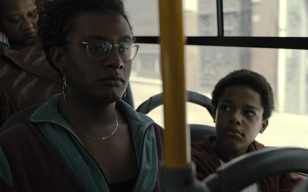 Cassandra (Liniker) no lado esquerdo e Gersinho (Gustavo Coelho) no lado direito em um ônibus