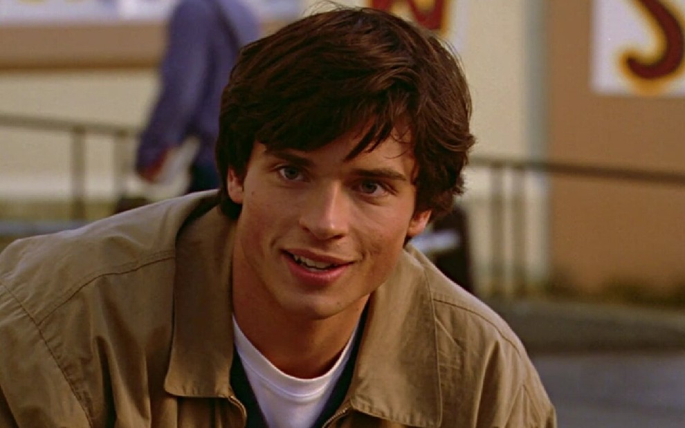 Clark (Tom Welling) de camisa branca e jaqueta marrom olhando para a esquerda em cena da série Smallville