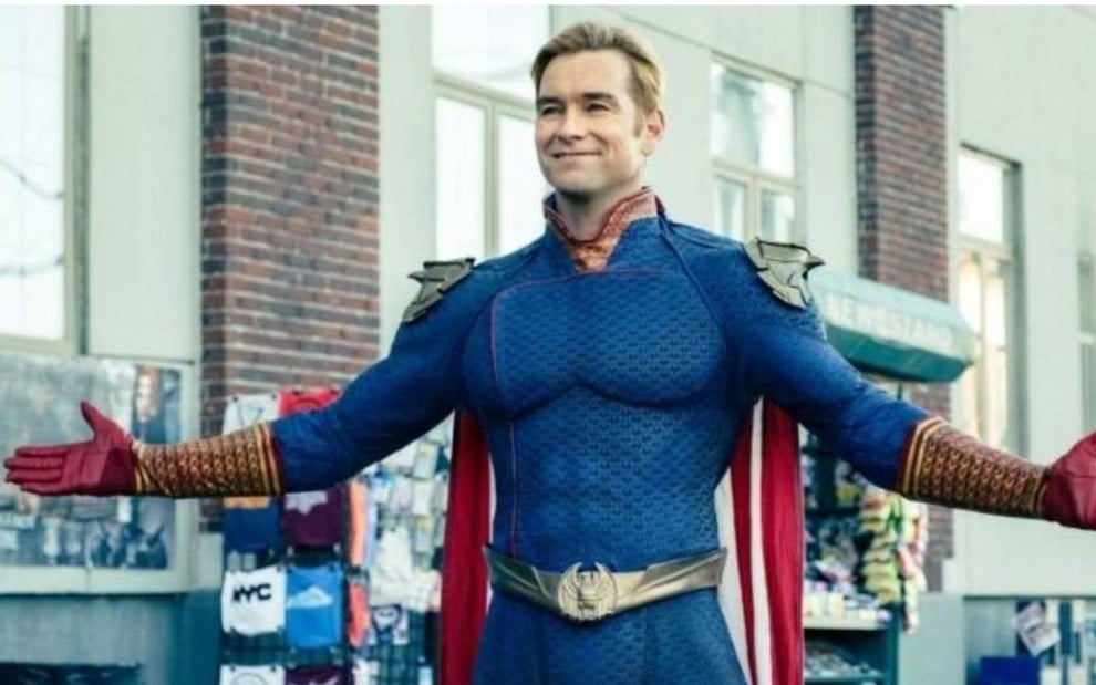 Capitão Pátria (Antony Starr) com uniforme azul de super-herói com sorriso no rosto e braços levantados em cena da série The Boys