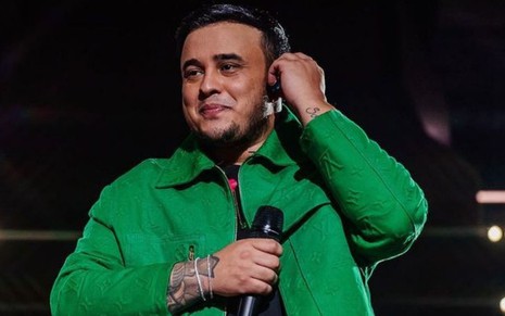 Imagem de Kauan com jaqueta verde e segurando microfone durante show