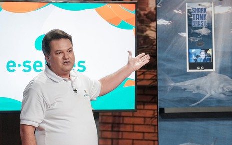 O empresário Sidney Monaco aponta para display com monitor, com expressão séria e camisa branca durante participação no Shark Tank Brasil