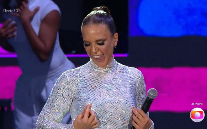 Com roupa prateada, Ivete Sangalo com as mãos nos seios e língua de fora