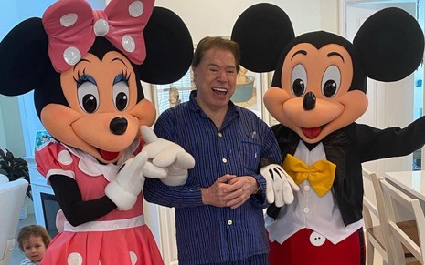 Silvio Santos sorri ao lado dos personagens Minnie e Mickey Mouse