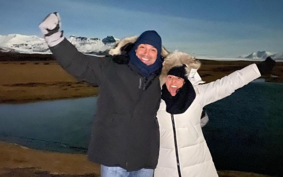De braços abertos, Tadeu Schmidt e a mulher Ana Cristina com roupas de frio em cenário polar