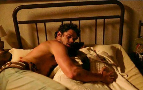 O ator José Loreto e a atriz Dira Paes como Tadeu e Filó em Pantanal; ele está deitado na cama abraçando a mulher, que está debaixo dos lençóis