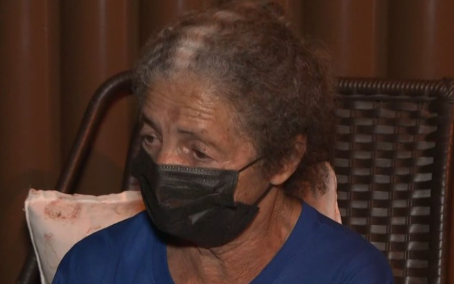 Dona Tereza olha para baixo, usa máscara preta e camiseta azul