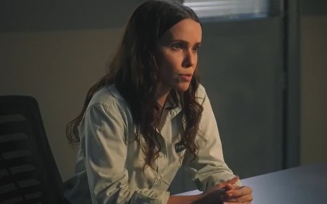 A atriz Débora Falabella com expressão séria, diante de mesa em sala de delegacia, em cena da novela Terra e Paixão
