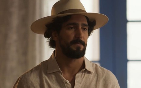 Renato Góes usa um chapéu e está com expressão séria em cena como Tertulinho na novela Mar do Sertão