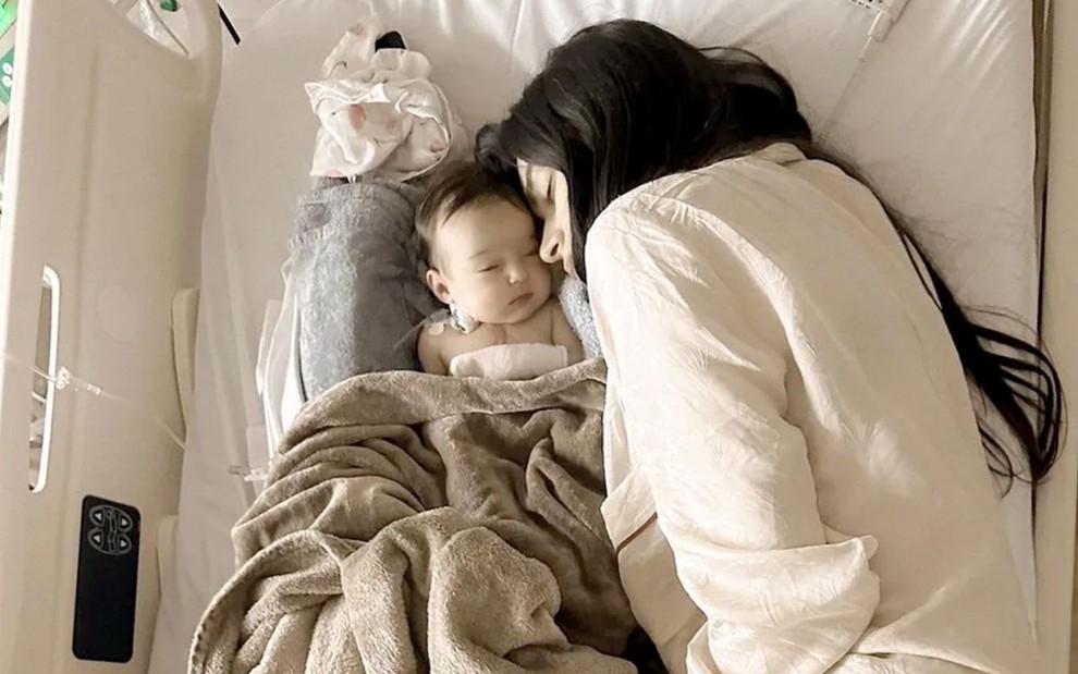 A atriz Thaila Ayala deitada em uma cama com a filha Tereza