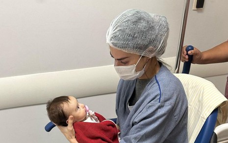 A atriz Thaila Ayala, com capote cirúrgico, com a filha Tereza no colo