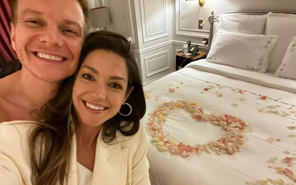 Michel Teló e Thaís Fersoza de rosto colado em quarto de hotel, com a cama coberta por pétalas de rosas