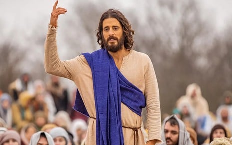 Caracterizado como Jesus, Jonathan Roumie ergue o braço direito enquanto discursa entre seguidores