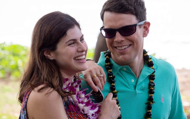 Os atores Alexandra Daddario e Jake Lacy abraçados, sorrindo, com colares havaianos, em cena externa da série The White Lotus