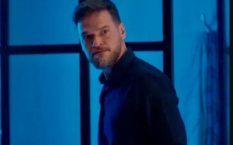Em cena de Vai na Fé, Emilio Dantas usa uma blusa preta e olha para alguém com raiva