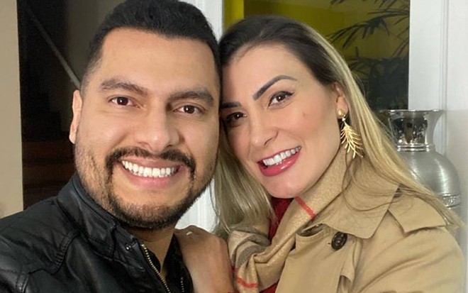 Thiago sorri, veste jaqueta preta e está ao lado de Andressa; ela sorri e veste um casaco bege