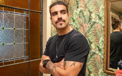 Caio Castro caracterizado como Pablo em Todas as Flores, com camiseta preta, olhando para a direita