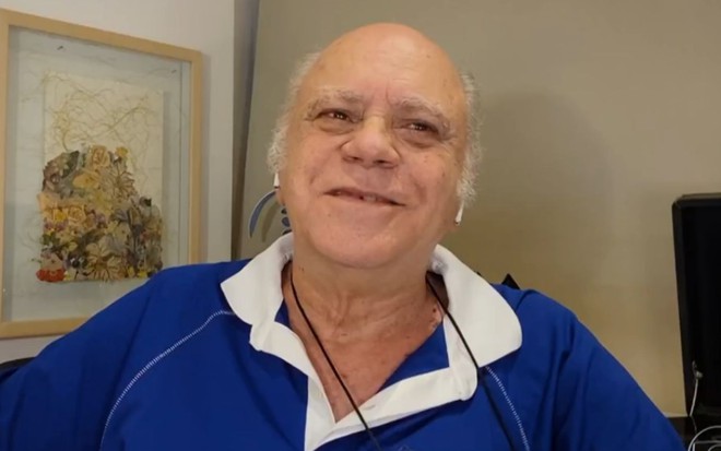 Tonico Pereira em entrevista ao programa Conversa com Bial. O ator veste uma camisa azul, com um óculos pendurado no pescoço e está um smeblante sorridente.