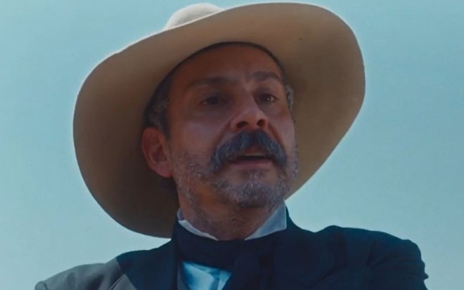 Alexandre Nero com expressão séria e usando chapéu em cena como Tonico na novela Nos Tempos do Imperador