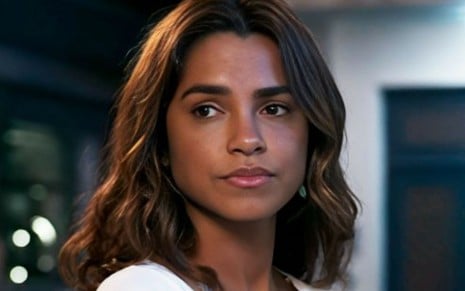 Em cena de Travessia, Lucy Alves usa uma blusa branca e está com a expressão de preocupada