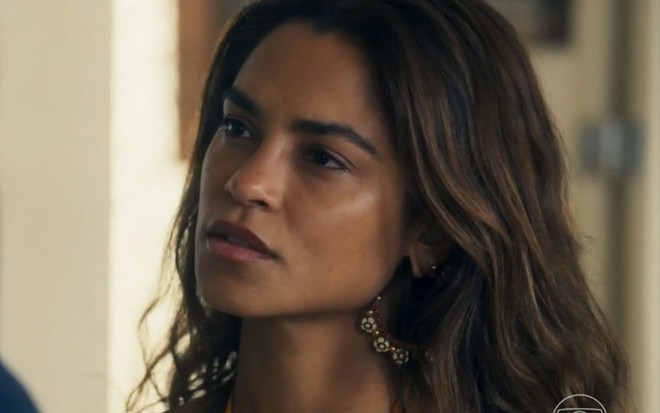 A atriz Lucy Alves como Brisa em Travessia; ela está de lado, olhando para frente com cara séria