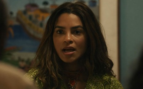 A atriz Lucy Alves como Brisa em Travessia; ela está olhando para frente com a boca semiaberta enquanto conversa