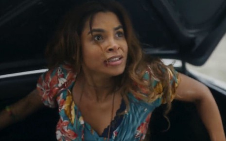A atriz Lucy Alves como Brisa em Travessia; ela está sentado dentro de um porta-malas, olhando para o lado com cara de assustada