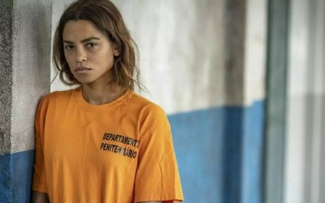 A atriz Lucy Alves com expressão séria e uniforme de detenta em cena de Travessia