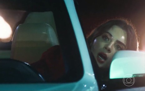 A atriz Jade Picon como Chiara em Travessia; ela está dirigindo, com a cabeça para fora do veículo e a boca semiaberta enquanto conversa