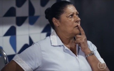 A atriz Luci Pereira com expressão pensativa, dedo na boca, olhando para a direita em cena de Travessia