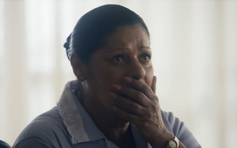 A atriz Luci Pereira com a mão na boca e expressão de espanto em cena de Travessia