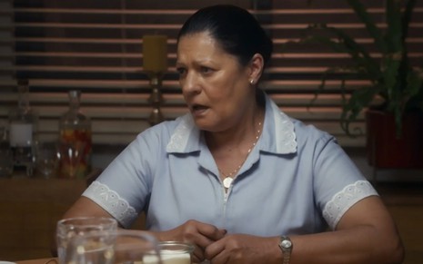 A atriz Luci Pereira com expressão de indignação, rosto voltado para a esquerda, com uniforme de empregada em cena de Travessia