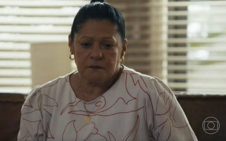 Em cena de Travessia, Luci Pereira esta usando blusa branca estampada e está com a expressão de tristeza