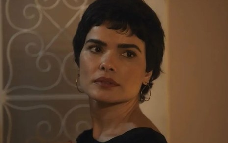 A atriz Vanessa Giácomo como Leonor em Travessia; ela está olhando para o lado com cara séria enquanto observa alguém