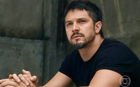 Em cena de Travessia, Romulo Estrela está com a expressão de tristeza; ele usa blusa preta